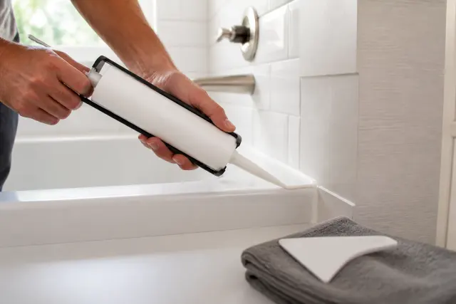 Fresh caulk being applied along the edge of a bathtub.