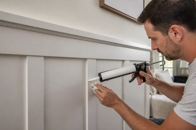 Applying paintable caulk along the edge of board and batten trim.